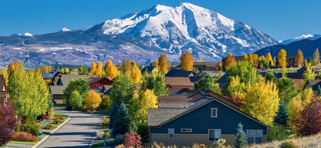 photograph of a colorado neighborhood with rocky mountains in background in early fall with trees looking green and gold.