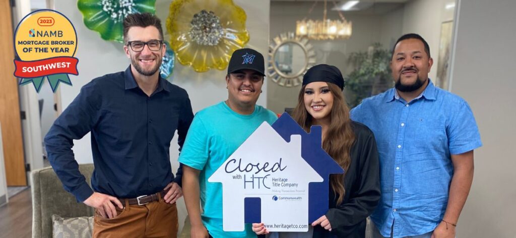 The Mortgage Architects loan officer with happy clients at closing appointment hodling up house cardboard cutout after signing contract for new home.