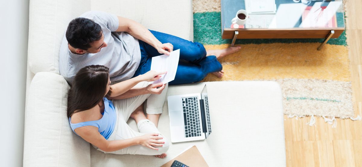 Couple sitting on a couch reviewing financial documents with a laptop open, discussing FHA loan options at home.