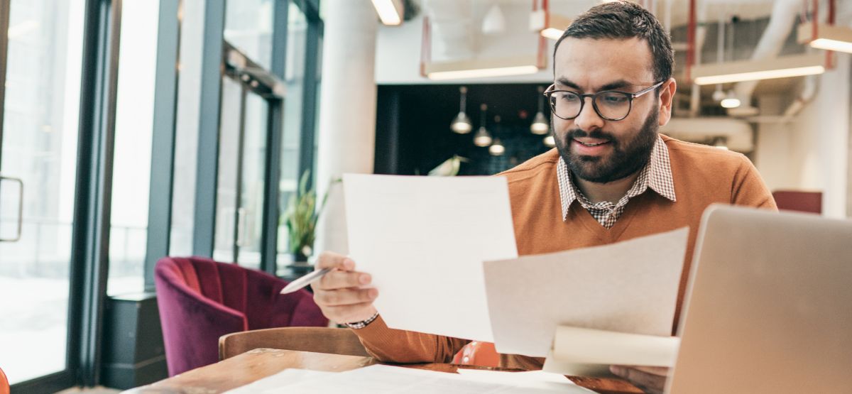 Man reviewing financial documents at a laptop in a modern office, preparing for student loan repayment planning.