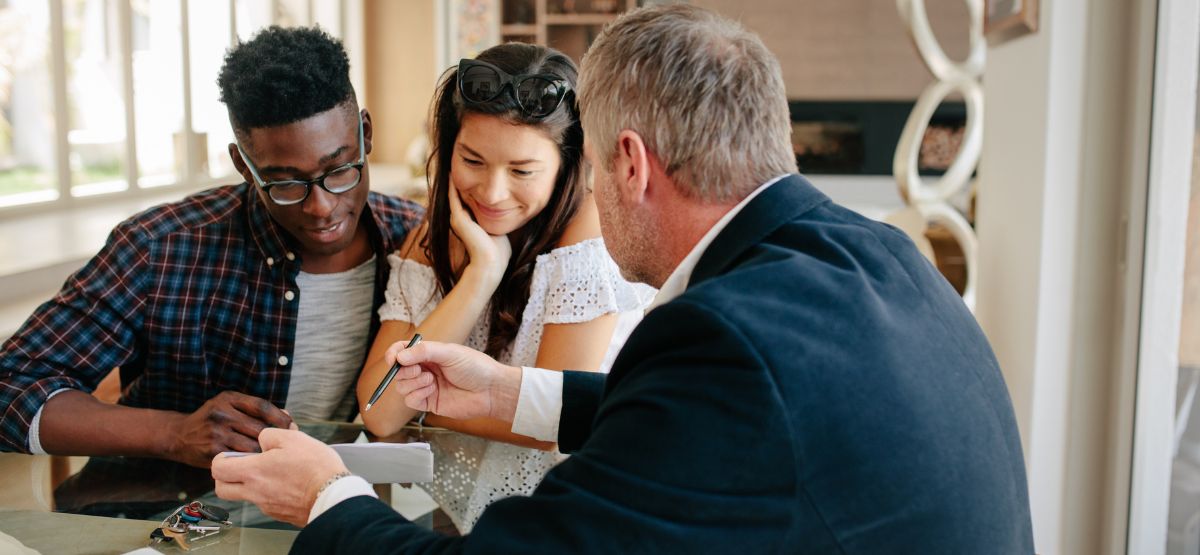 Couple reviewing documents with a real estate agent, highlighting the guidance and support a buyer’s agent provides during the home buying process.
