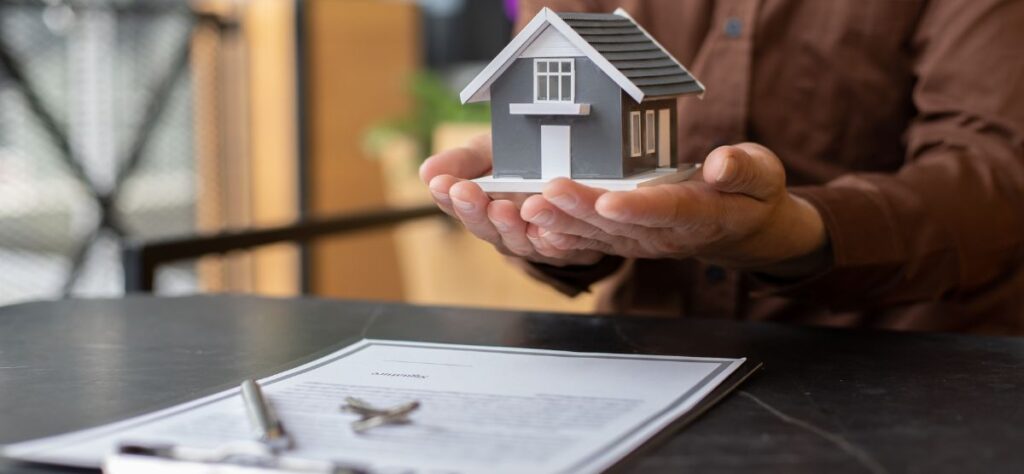 A mortgage broker holding a house model above ITIN loan paperwork.