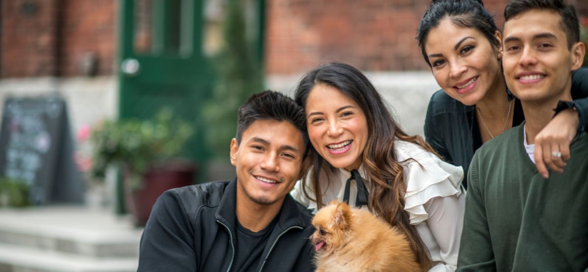 Smiling Hispanic family with their dog sitting outside their home, representing ITIN mortgage programs that support family homeownership.