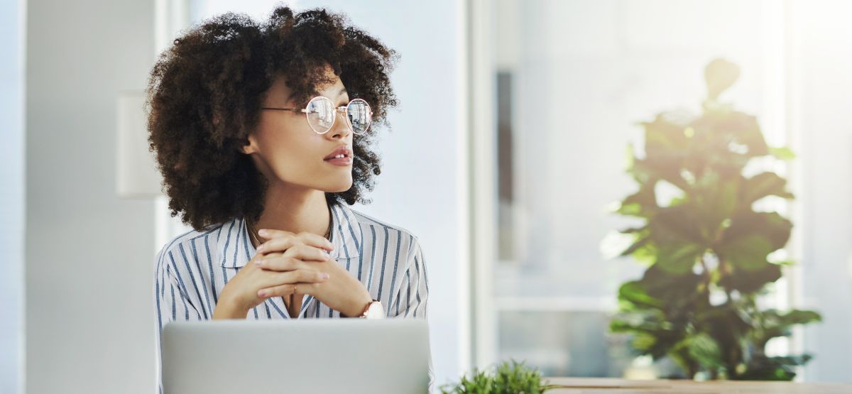 Thoughtful woman wearing glasses sitting at a desk with a laptop, symbolizing careful consideration of mortgage discount points and financial decisions.